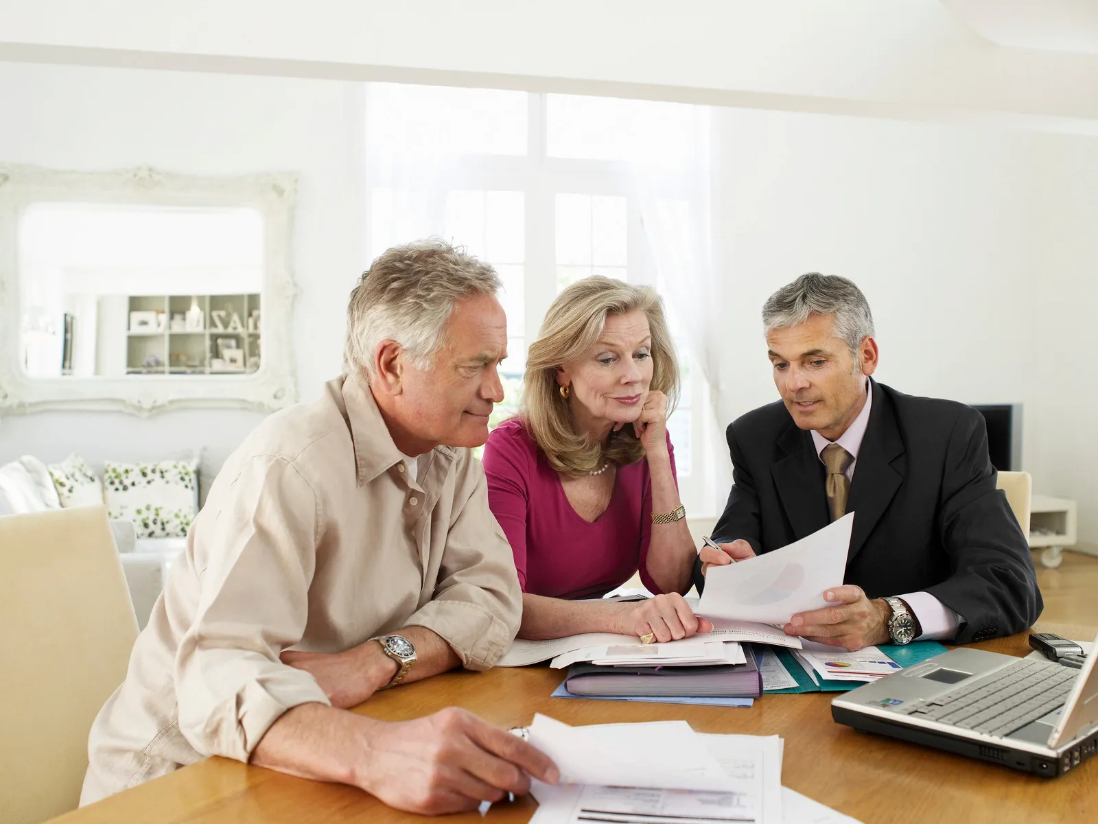 an older couple sits at a table with a businessman who goes over paperwork with them